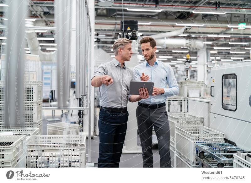 Zwei Geschäftsleute mit Tablette im Gespräch in einer modernen Fabrik Arbeitskollege Arbeitskollegen Kollege Partner Partnerschaften Job Berufe Berufstätigkeit