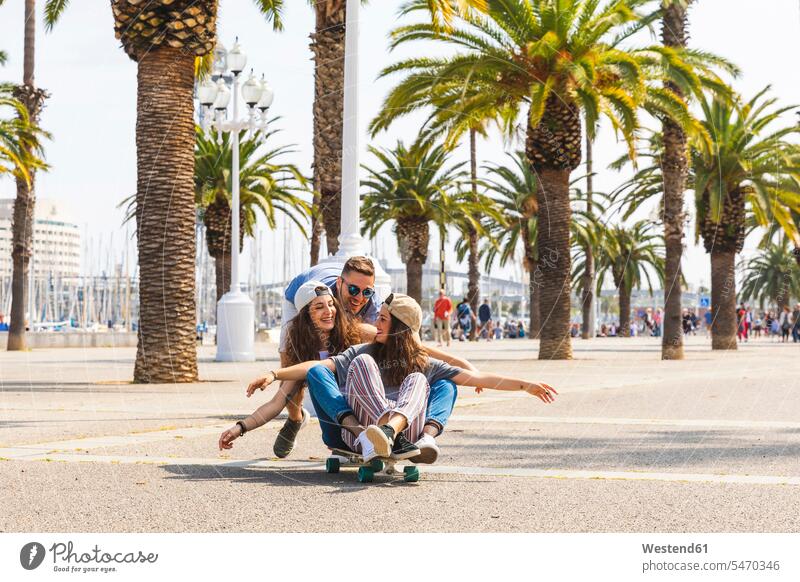 Sorglose Freunde, die sich auf einer Promenade mit Palmen mit einem Skateboard vergnügen Unbeschwert glücklich Glück glücklich sein glücklichsein Promenaden