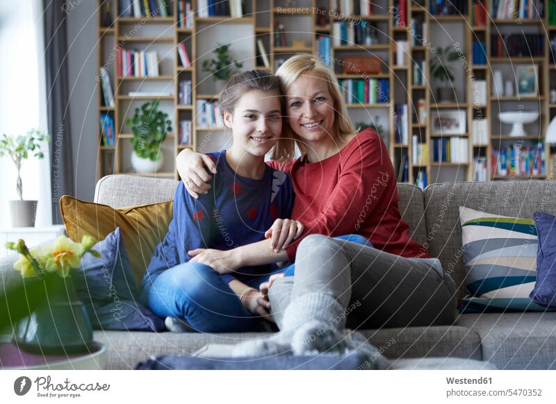 Mutter und halbwüchsige Tochter sitzen auf dem Sofa und legen die Arme um Couches Liege Sofas Verständnis verstehen verständnisvoll Kindheit offenes Lächeln