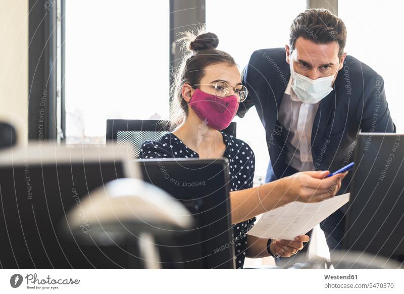 Geschäftsleute, die eine Gesichtsmaske tragen, diskutieren während der Arbeit im Büro Farbaufnahme Farbe Farbfoto Farbphoto Innenaufnahme Innenaufnahmen innen
