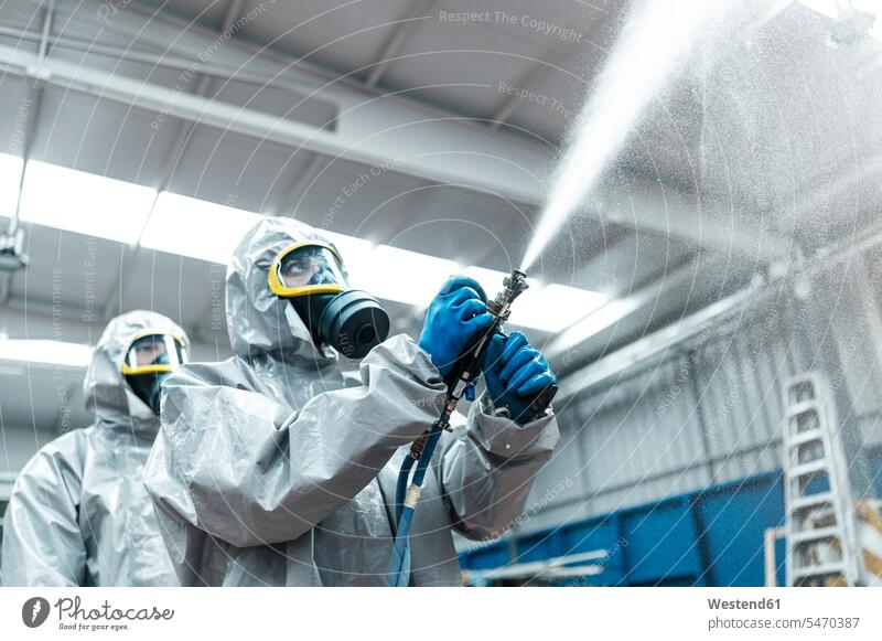 Niedrigwinkelansicht von Sanitärarbeitern, die in einem Lagerhaus Chemikalien aus Schläuchen versprühen Farbaufnahme Farbe Farbfoto Farbphoto Coronavirus