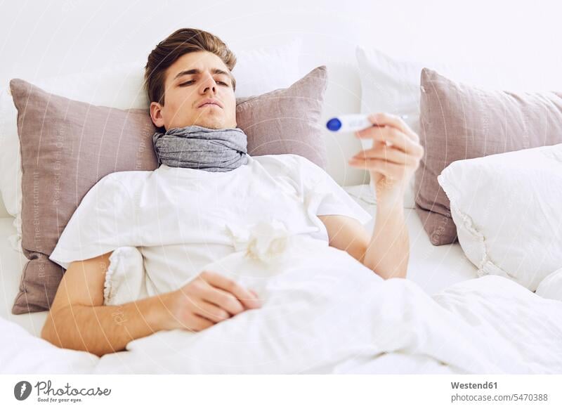Kranker Mann untersucht Temperatur mit Thermometer, während er zu Hause im Bett liegt Farbaufnahme Farbe Farbfoto Farbphoto Deutschland Innenaufnahme