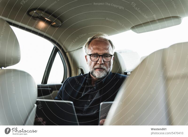 Ein reifer Geschäftsmann sitzt auf dem Rücksitz im Auto und benutzt ein digitales Tablet Wagen PKWs Automobil Autos Ruecksitz Ruecksitze Rücksitze Smartphone