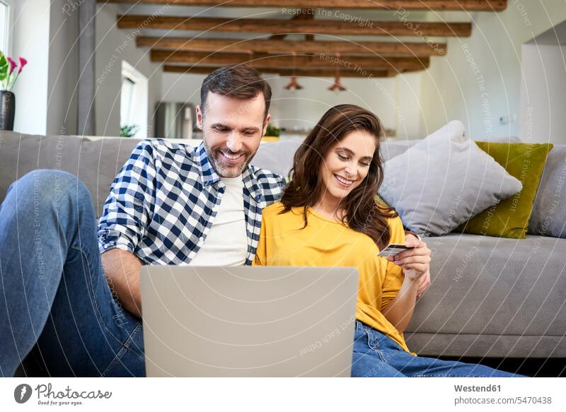 Paar, das im Wohnzimmer sitzt, einen Laptop benutzt und eine Online-Zahlung mit seiner Kreditkarte vornimmt EC-Karte Kreditkarten Laptop benutzen