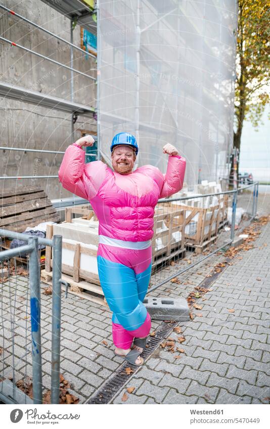 Porträt eines stolzen Mannes mit rosa Bodybuilder-Kostüm und Schutzhelm auf der Baustelle Leute Menschen People Person Personen Europäisch Kaukasier kaukasisch