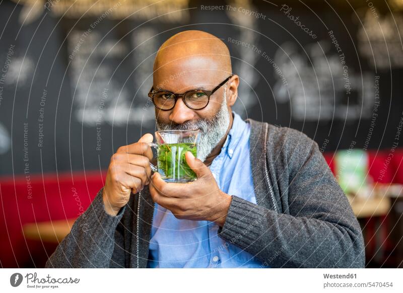 Porträt eines lächelnden Mannes mit einem Glas Tee in einem Café Männer männlich Portrait Porträts Portraits Cafe Kaffeehaus Bistro Cafes Kaffeehäuser Tees