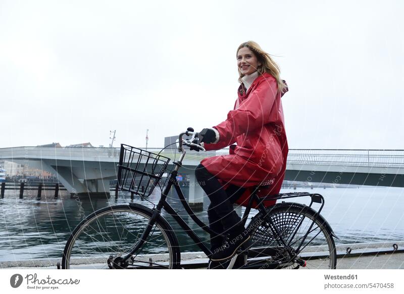 Dänemark, Kopenhagen, glückliche Frau fährt Fahrrad am Wasser bei regnerischem Wetter Bikes Fahrräder Räder Rad weiblich Frauen Glück glücklich sein