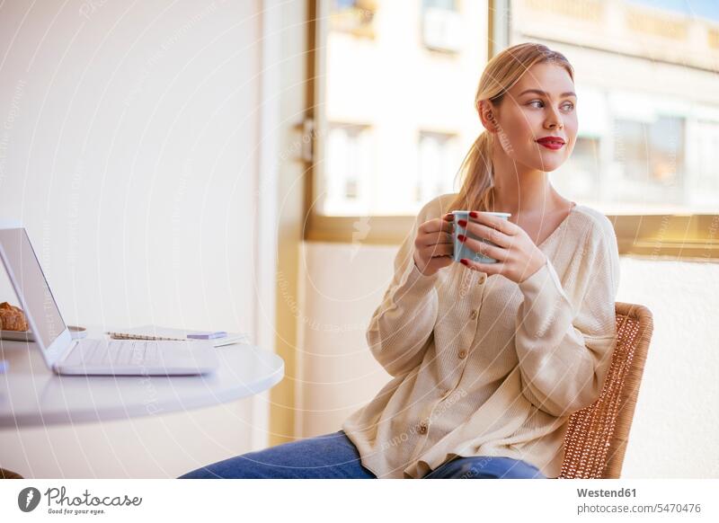 Blonde Frau mit einer Tasse Kaffee, die aus dem Fenster schaut Kaffeetasse Kaffeetassen attraktiv schoen gut aussehend schön Attraktivität gutaussehend hübsch