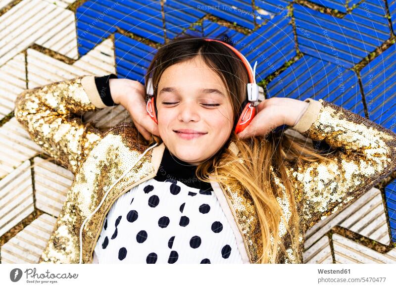 Porträt eines glücklichen Mädchens mit goldener Paillettenjacke, das mit Kopfhörern Musik hört Jacke Jacken Portrait Porträts Portraits weiblich goldfarben