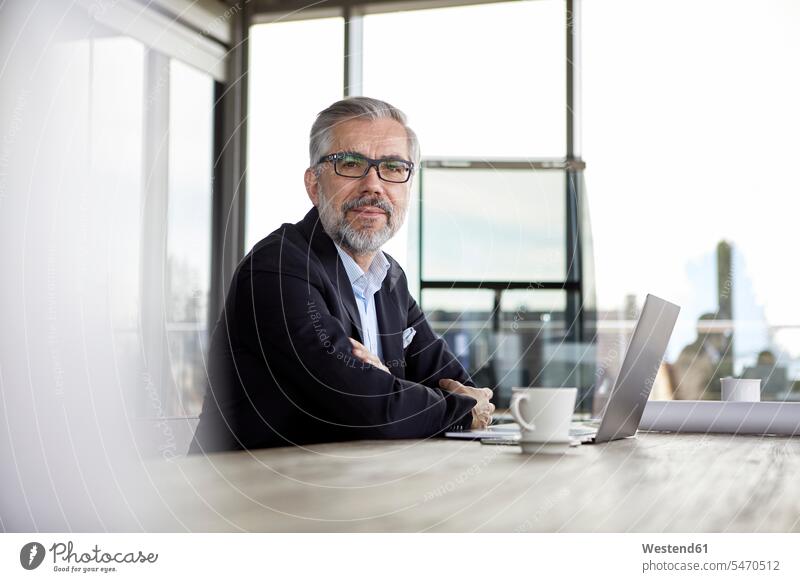 Porträt eines selbstbewussten Geschäftsmannes mit Laptop am Schreibtisch im Büro Portrait Porträts Portraits Arbeitstisch Schreibtische Notebook Laptops