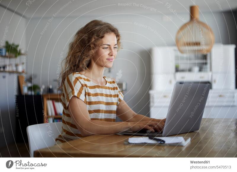 Mittlere erwachsene Frau, die am Laptop arbeitet, während sie zu Hause am Tisch sitzt Farbaufnahme Farbe Farbfoto Farbphoto Innenaufnahme Innenaufnahmen innen