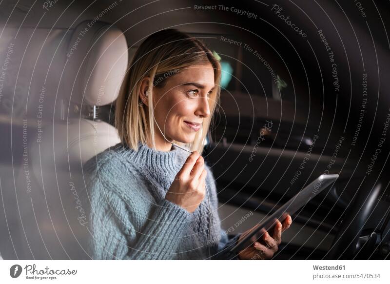 Lächelnde junge Frau mit Tablette und Kopfhörern in einem Auto Transport Transportwesen KFZ Verkehrsmittel Automobil Autos PKW PKWs Wagen Arbeit hoeren sitzend
