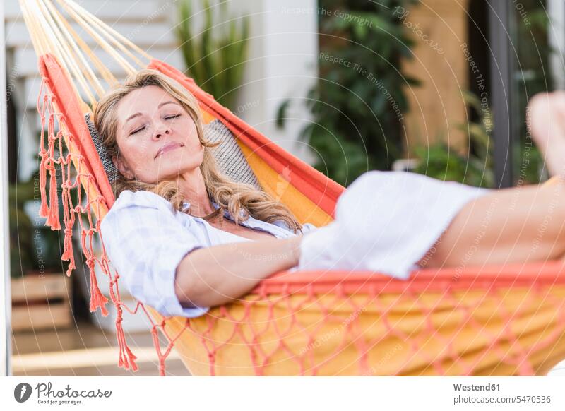 Porträt einer reifen Frau mit geschlossenen Augen, die sich in der Hängematte auf der Terrasse entspannt Hängematten entspannen relaxen geniessen Genuss liegend