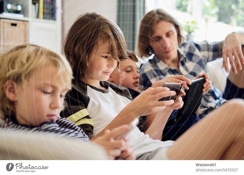 Vater sieht Jungen an, die auf Smartphones und digitalen Tablets im Wohnzimmer Spiele spielen Farbaufnahme Farbe Farbfoto Farbphoto Innenaufnahme Innenaufnahmen