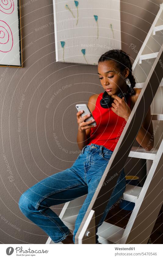 Teenagerin benutzt Smartphone, während sie zu Hause auf der Leiter sitzt Farbaufnahme Farbe Farbfoto Farbphoto Innenaufnahme Innenaufnahmen innen drinnen Tag