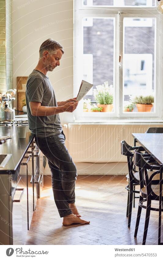Reifer Mann liest zu Hause in der Küche Zeitung Leute Menschen People Person Personen Alleinstehende Alleinstehender Singles Unverheiratete Unverheirateter