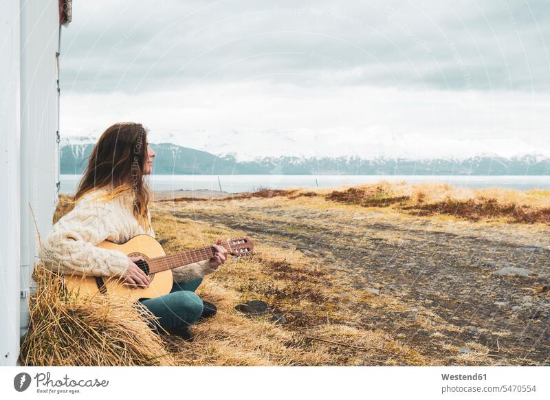 Island, Frau sitzt in ländlicher Landschaft und spielt Gitarre Gitarren Landschaften weiblich Frauen spielen Republik Island sitzen sitzend auf dem Land