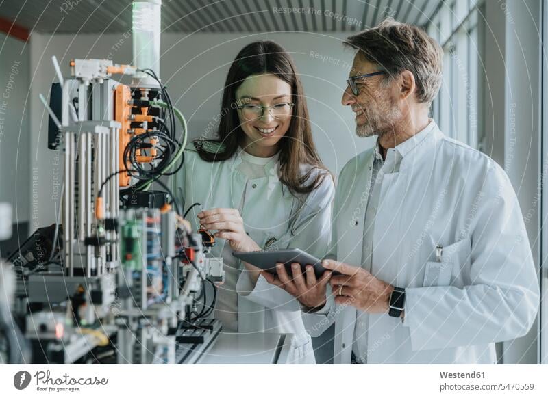 Reifer Mann zeigt einer Kollegin ein digitales Tablett, während er im Labor an einer Maschine steht Farbaufnahme Farbe Farbfoto Farbphoto Innenaufnahme