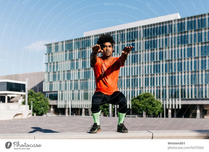 Junger Mann beim Sport, Kniebeugen T-Shirts Kopfhoerer hoeren Muße Anreiz Ansporn Antrieb motivieren motiviert außen draußen im Freien staedtisch städtisch