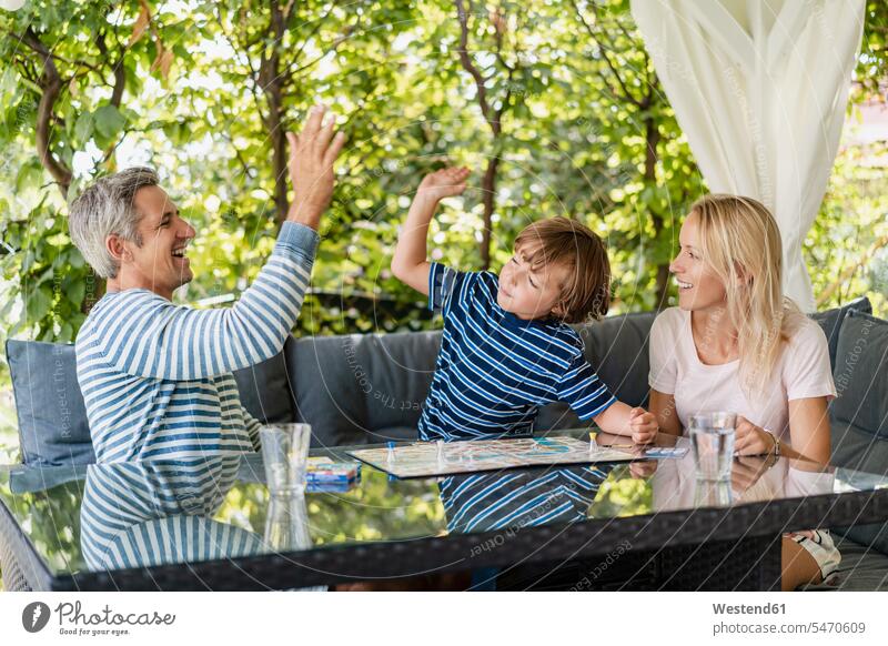 Glückliche Vater und Sohn nach gewonnenem Spiel auf der Terrasse Spiele Gesellschaftsspiele Brettspiele Jubel gewinnen sitzend sitzt sommerlich Sommerzeit