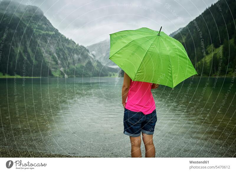 Reife Frau steht mit grünem Regenschirm in der Regenzeit am Vilsalpseeufer Farbaufnahme Farbe Farbfoto Farbphoto Österreich Außenaufnahme außen draußen