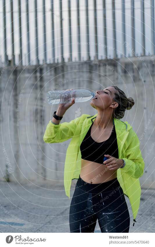 Sportliche Frau trinkt aus einer Wasserflasche Uhren Armbanduhren gelbe gelber gelbes stehend steht Leistungen Fit gesund Gesundheit erfrischen erfrischend