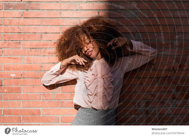 Porträt einer schönen jungen Frau mit Afrofrisur an Backsteinmauer bei Sonnenschein Afrolook Afros Afro-look Sonnenlicht Portrait Porträts Portraits weiblich