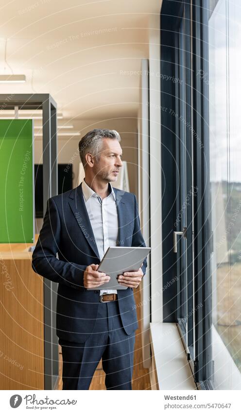 Reifer Geschäftsmann mit Tablett im Büro, der aus dem Fenster schaut Job Berufe Berufstätigkeit Beschäftigung Jobs geschäftlich Geschäftsleben Geschäftswelt