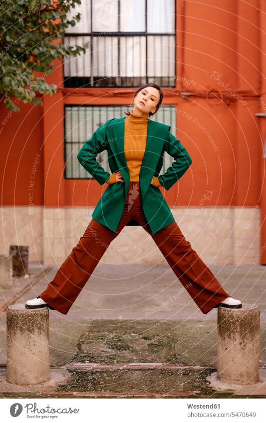 Junge Frau in grüner Jacke steht auf Pollern gegen Gebäude in der Stadt Farbaufnahme Farbe Farbfoto Farbphoto Spanien Freizeitkleidung Freizeitbekleidung casual