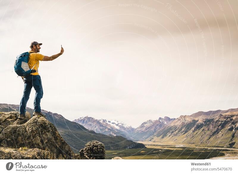 Ein reifer Mann, der sich mit einem Smartphone selbstständig macht, während er auf einem Felsen gegen den Himmel steht, Patagonien, Argentinien Südamerika