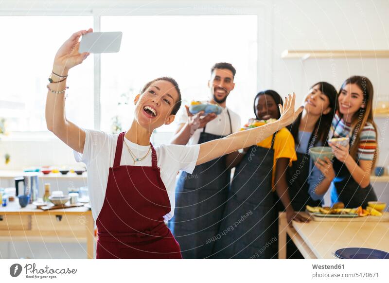 Verspielter Ausbilder macht ein Selfie mit Freunden in einem Kochworkshop Ausbilderin kochen Kurs Kochkurs Küche Freundschaft lachen halten Smartphone verspielt