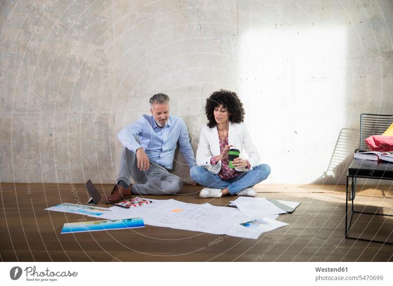 Geschäftsmann und Geschäftsfrau sitzen auf dem Boden in einem Loft und diskutieren Dokumente sprechen reden Businessmann Businessmänner Geschäftsmänner