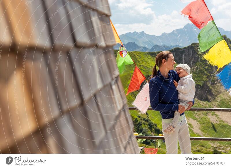 Deutschland, Bayern, Oberstdorf, glückliche Mutter mit kleiner Tochter auf einer Berghütte umgeben von Wimpeln Töchter Berghütten Berghuette Hütte tragen