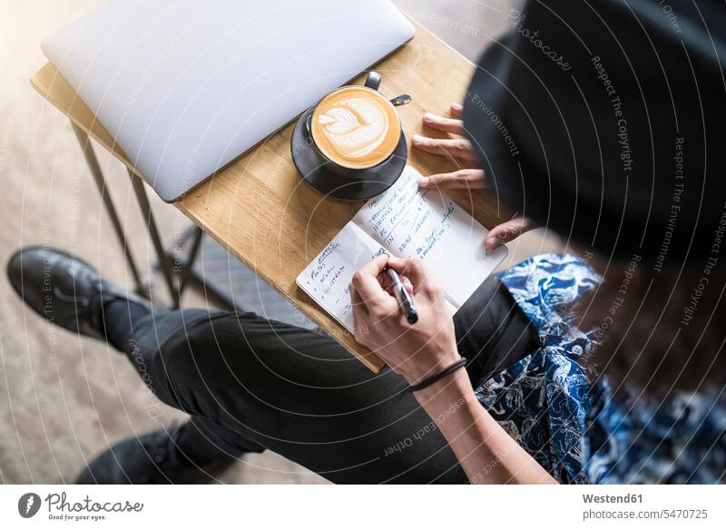 Künstler schreibt in einem Cafe mit Kaffee und Laptop auf dem Tisch in ein Notizbuch Kaffeehaus Bistro Cafes Café Cafés Kaffeehäuser Notizbücher Notizbuecher