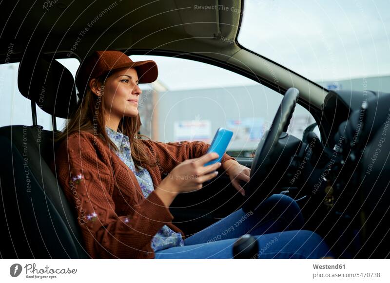 Junge Frau benutzt Mobiltelefon, während sie im Auto sitzt Farbaufnahme Farbe Farbfoto Farbphoto Tag Tageslichtaufnahme Tageslichtaufnahmen Tagesaufnahme am Tag