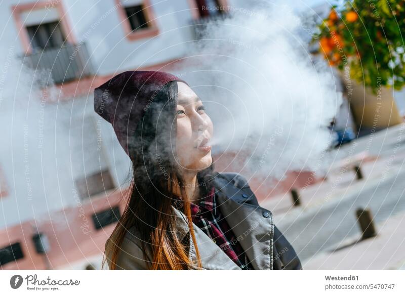 Junge Frau bläst den Rauch einer elektronischen Zigarette aus weiblich Frauen ausblasen auspusten Qualm E-Zigarette elektrische Zigarette Portrait Porträts