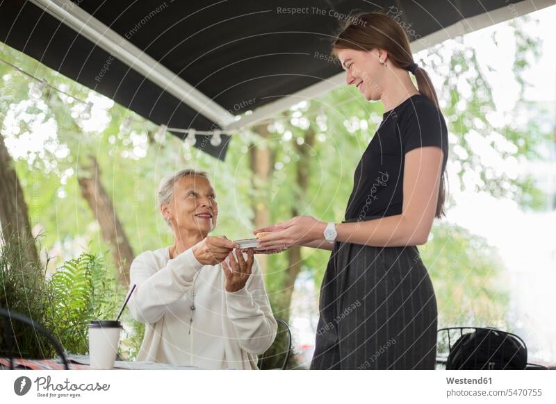 Kellnerin übergibt Teller an lächelnde ältere Frau in einem Straßencafé geben überreichen ueberreichen uebergeben übergeben Seniorin Seniorinnen alt Straßencafe