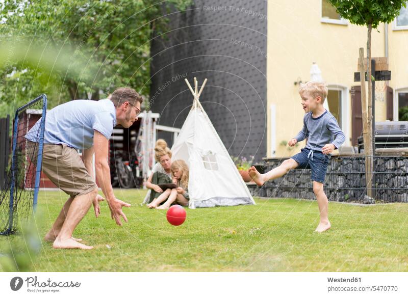 Mann und Sohn spielen Fußball, während die Frau am Wochenende mit der Tochter im Zelt im Hinterhof sitzt Farbaufnahme Farbe Farbfoto Farbphoto Deutschland