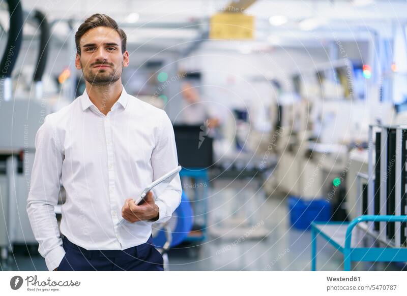 Selbstbewusster junger Geschäftsmann hält digitales Tablet, während er in beleuchteter Fabrik steht Farbaufnahme Farbe Farbfoto Farbphoto Innenaufnahme