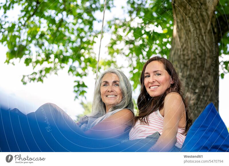Porträt von zwei lächelnden Frauen, die sich auf einem Hängebett im Garten entspannen Portrait Porträts Portraits hängen Bett Betten Gärten Gaerten entspannt