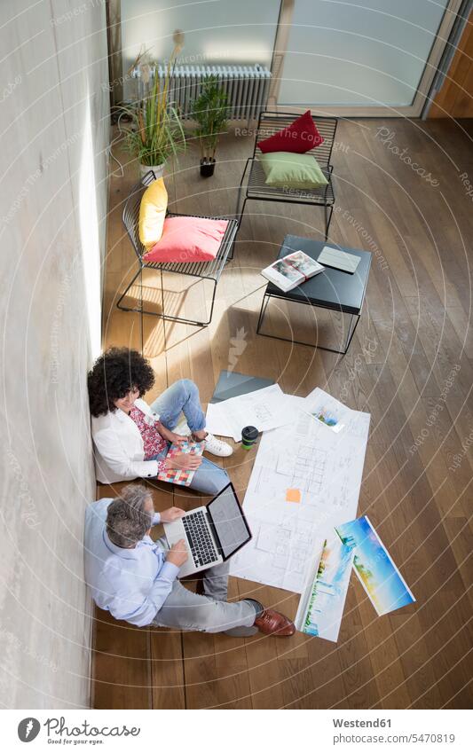 Geschäftsmann und Geschäftsfrau sitzen auf dem Boden in einem Loft arbeiten mit Laptop und Dokumente sitzend sitzt Unterlagen Arbeit Böden Boeden Businessmann