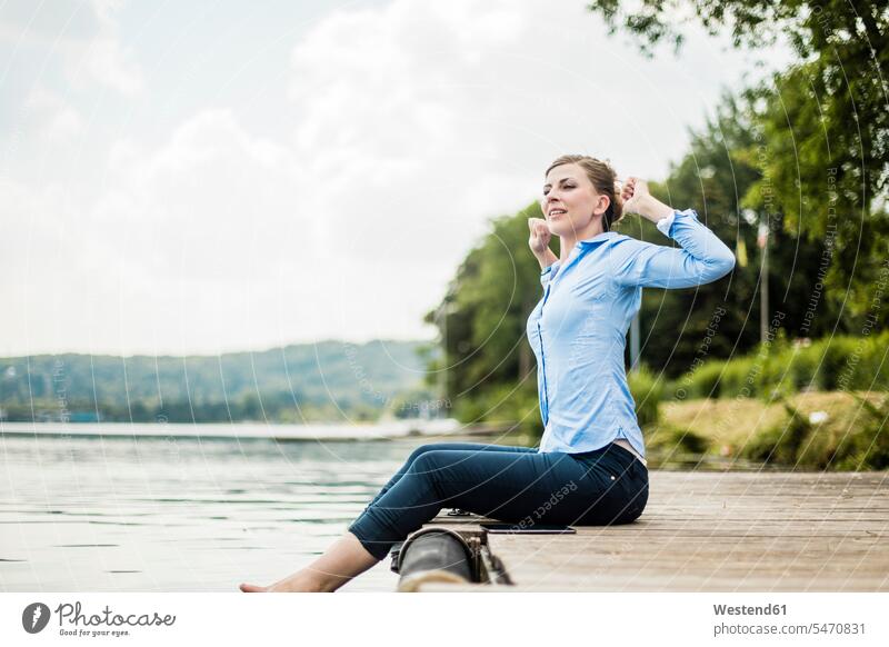 Frau sitzt auf Steg an einem See mit Füßen im Wasser Stege Anlegestelle weiblich Frauen Fuß Fuss sitzen sitzend Seen Erwachsener erwachsen Mensch Menschen Leute