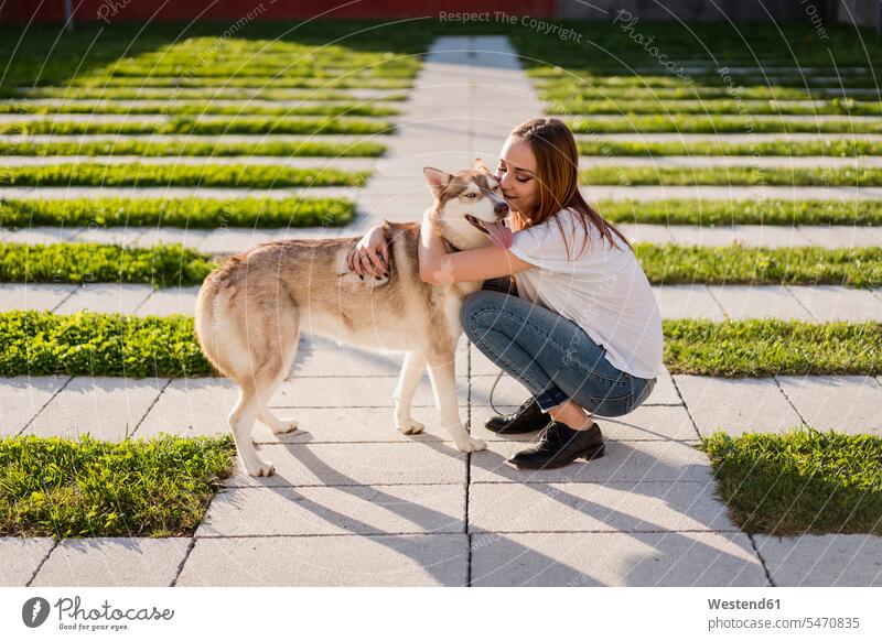 Glückliche junge Frau kuschelt mit ihrem Hund im Freien Tiere Tierwelt Haustiere Hunde T-Shirts Arm umlegen Umarmung Umarmungen abends Jahreszeiten sommerlich