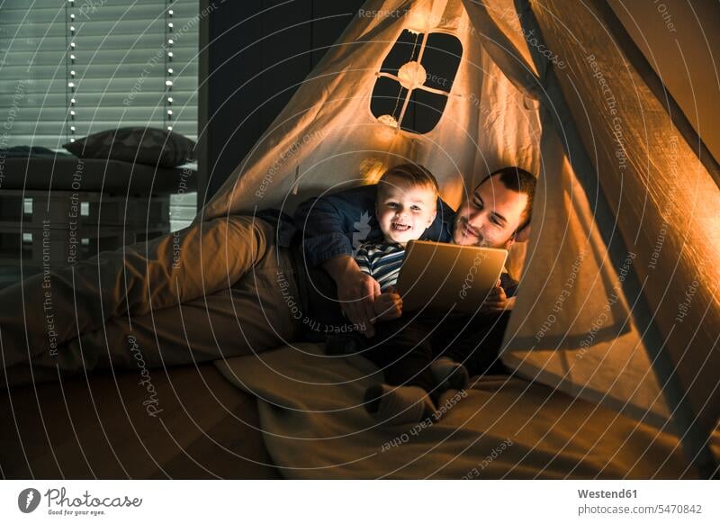 Vater und Sohn teilen sich ein Tablet in einem dunklen Zelt zu Hause Teilen Sharing dunkel Zelte liegen liegend liegt Zuhause daheim Tablet Computer Tablet-PC
