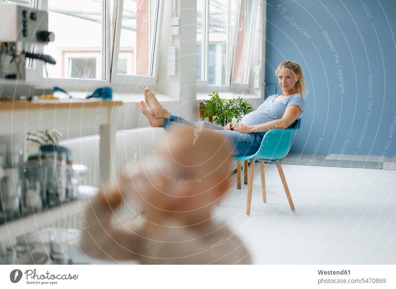 Schwangere Frau sitzt auf einem Stuhl am Fenster mit Kleinkind im Vordergrund sitzen sitzend schwanger schwangere Frau Stuehle Stühle weiblich Frauen