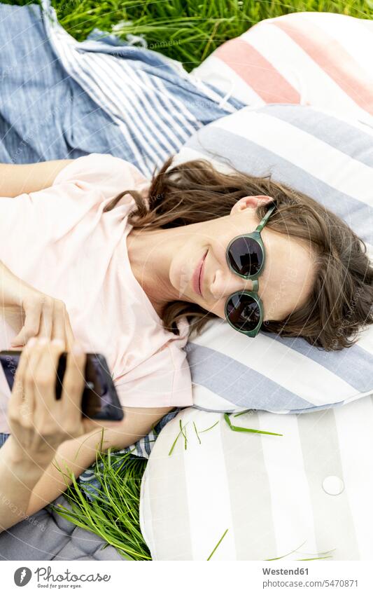 Entspannte Frau, die auf einer Wiese liegt und ein Mobiltelefon benutzt Textnachricht Leute Menschen People Person Personen erwachsen reifer Erwachsener