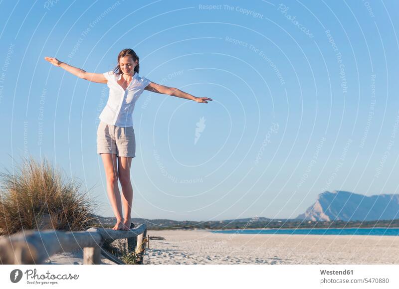 Lächelnde Frau balanciert auf einem Zaun am Strand, Sardinien, Italien ausgeglichen Ausgeglichenheit Gleichgewicht Balance entspannen relaxen gehend geht Muße