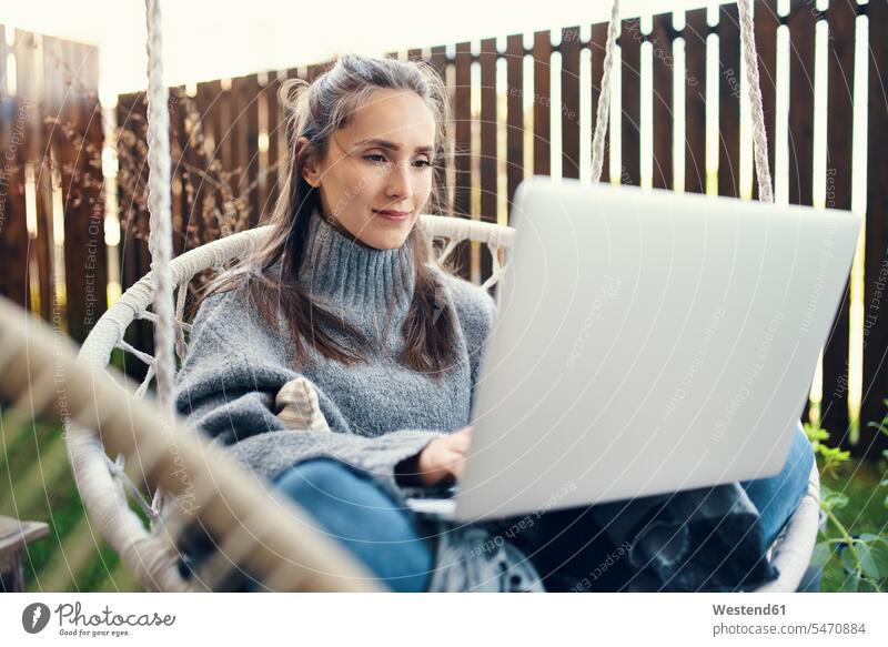 Schöne junge Frau benutzt Laptop, während sie im Garten auf der Schaukel sitzt Farbaufnahme Farbe Farbfoto Farbphoto Freizeitbeschäftigung Muße Zeit Zeit haben