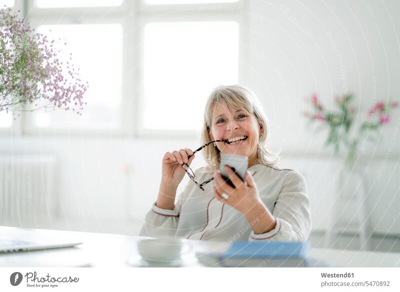 Porträt einer glücklichen reifen Geschäftsfrau, die ihr Handy am Schreibtisch hält Glück glücklich sein glücklichsein Geschäftsfrauen Businesswomen