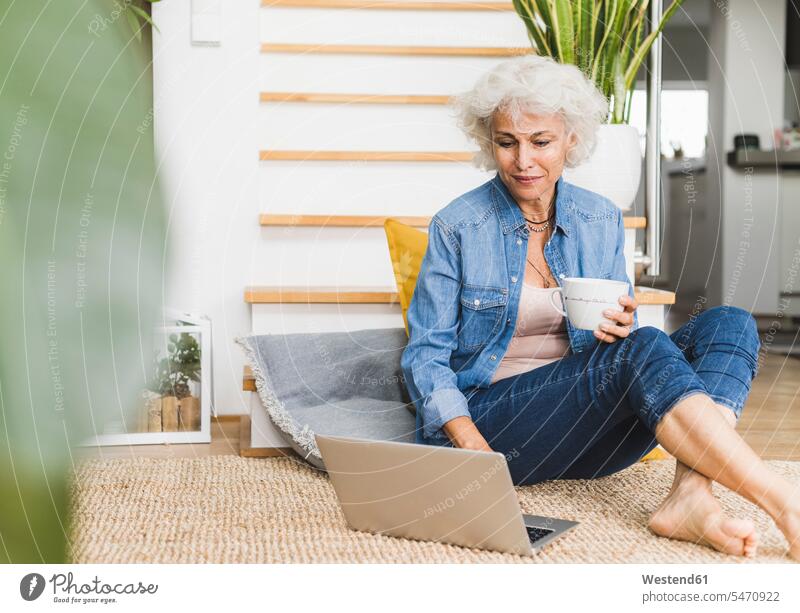 Reife Frau arbeitet am Laptop, während sie zu Hause sitzt Farbaufnahme Farbe Farbfoto Farbphoto Innenaufnahme Innenaufnahmen innen drinnen Tag